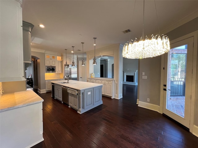 kitchen with sink, built in appliances, decorative light fixtures, dark hardwood / wood-style floors, and an island with sink