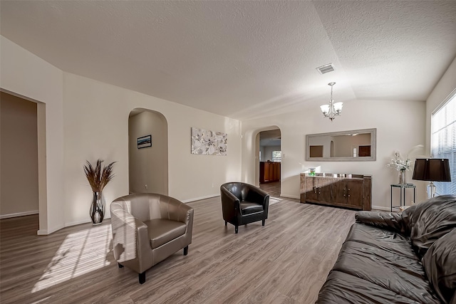 living room featuring a textured ceiling, hardwood / wood-style floors, lofted ceiling, and an inviting chandelier