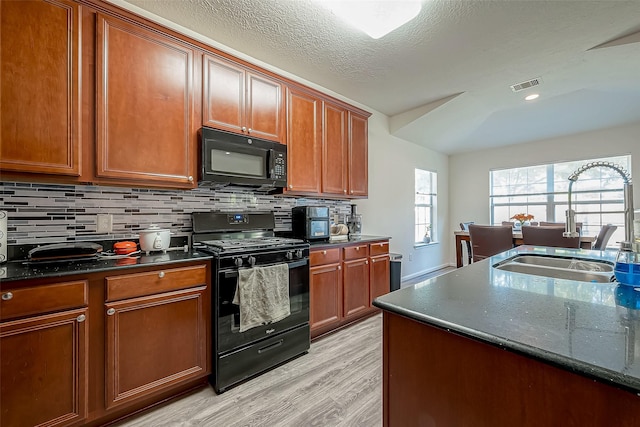 kitchen with sink, light hardwood / wood-style flooring, backsplash, dark stone counters, and black appliances