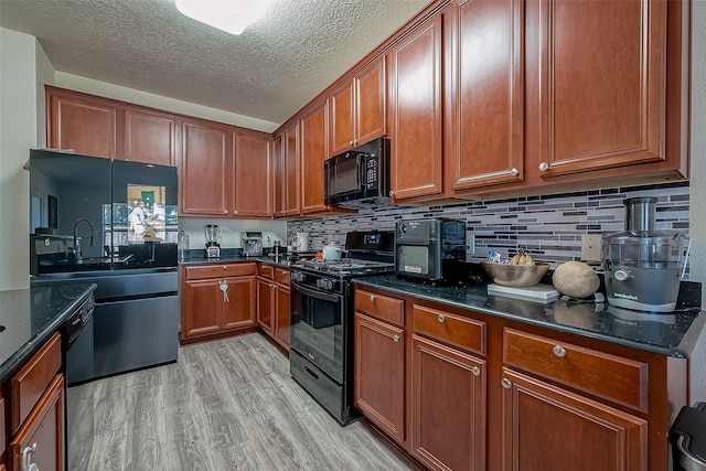 kitchen featuring black appliances, light hardwood / wood-style floors, dark stone counters, and tasteful backsplash