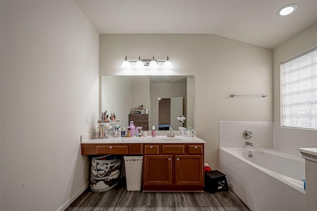 bathroom with a tub to relax in, a textured ceiling, vanity, hardwood / wood-style flooring, and lofted ceiling