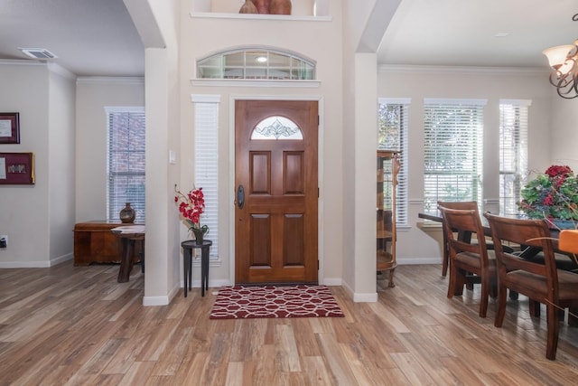 foyer entrance with light hardwood / wood-style floors, an inviting chandelier, and crown molding