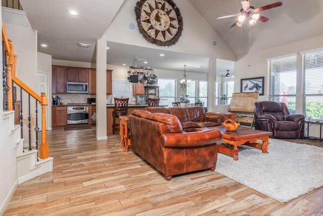 living room featuring light hardwood / wood-style flooring, high vaulted ceiling, and ceiling fan with notable chandelier