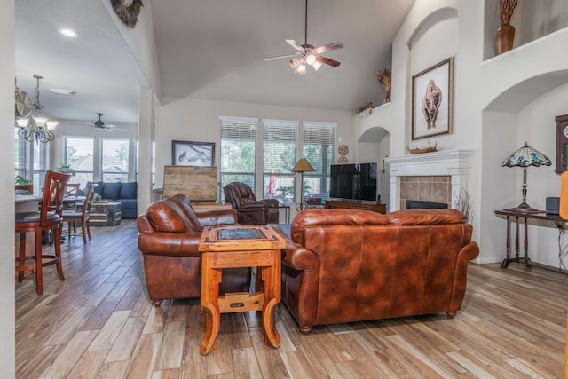 living room with ceiling fan with notable chandelier, light wood-type flooring, a fireplace, and high vaulted ceiling