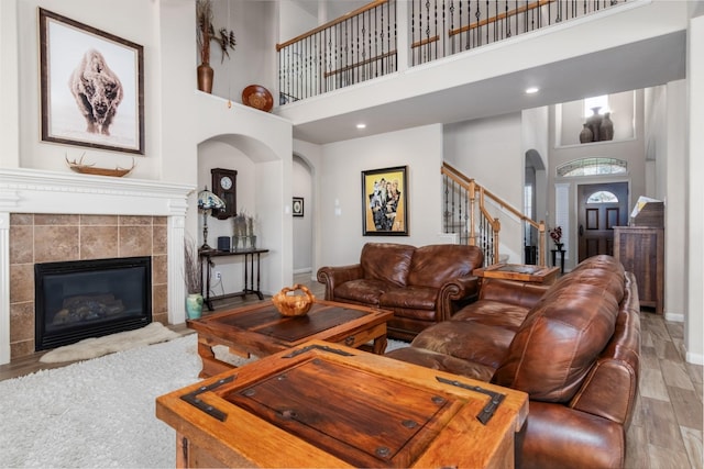 living room with a tiled fireplace, a towering ceiling, and wood-type flooring