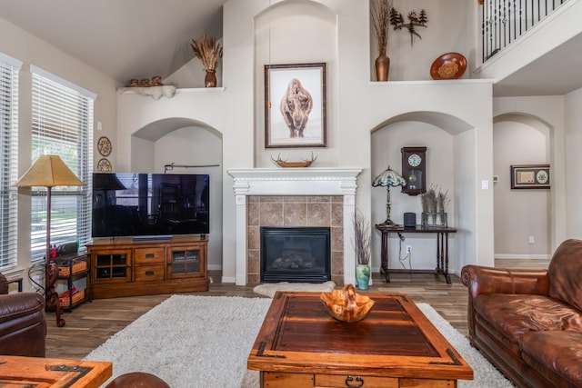 living room featuring a tile fireplace, wood-type flooring, and a high ceiling