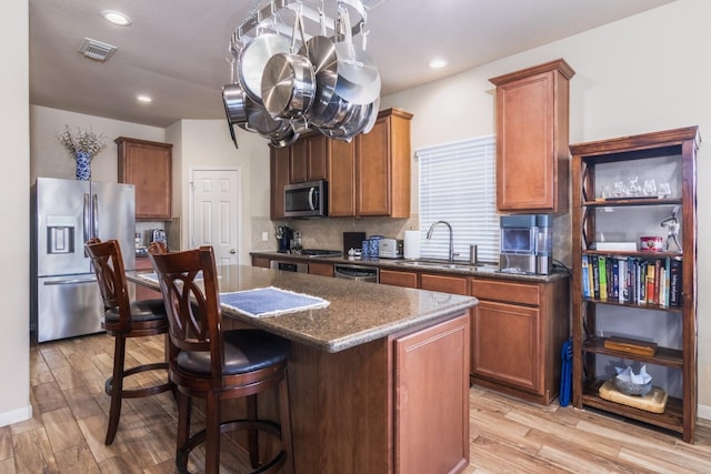 kitchen with sink, a center island, dark stone countertops, light hardwood / wood-style floors, and appliances with stainless steel finishes