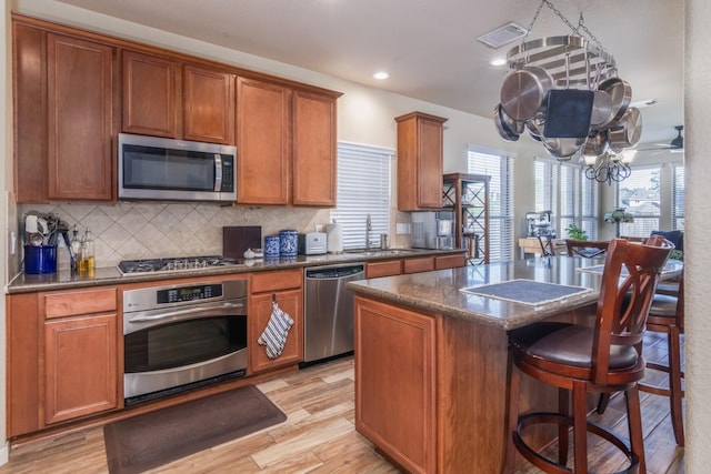 kitchen featuring backsplash, a center island with sink, sink, light wood-type flooring, and stainless steel appliances