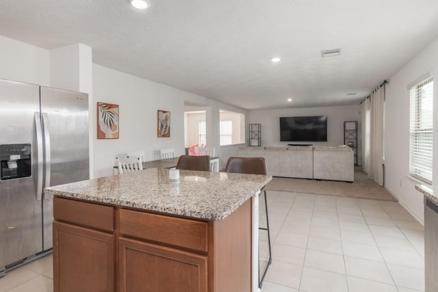 kitchen with a kitchen bar, light stone counters, a center island, and stainless steel refrigerator with ice dispenser