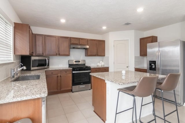 kitchen with sink, stainless steel appliances, light stone counters, a breakfast bar, and a kitchen island