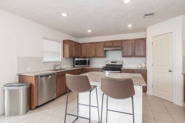 kitchen with a center island, sink, light tile patterned floors, appliances with stainless steel finishes, and light stone counters