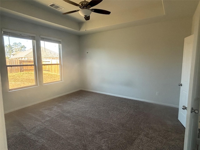 unfurnished room with a raised ceiling, ceiling fan, and dark colored carpet