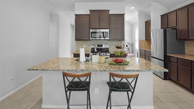 kitchen featuring a kitchen breakfast bar, light stone counters, light tile patterned flooring, and appliances with stainless steel finishes