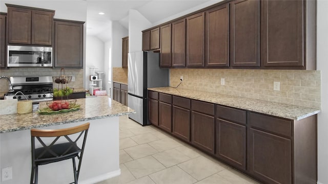 kitchen featuring light stone countertops, appliances with stainless steel finishes, a breakfast bar, and decorative backsplash