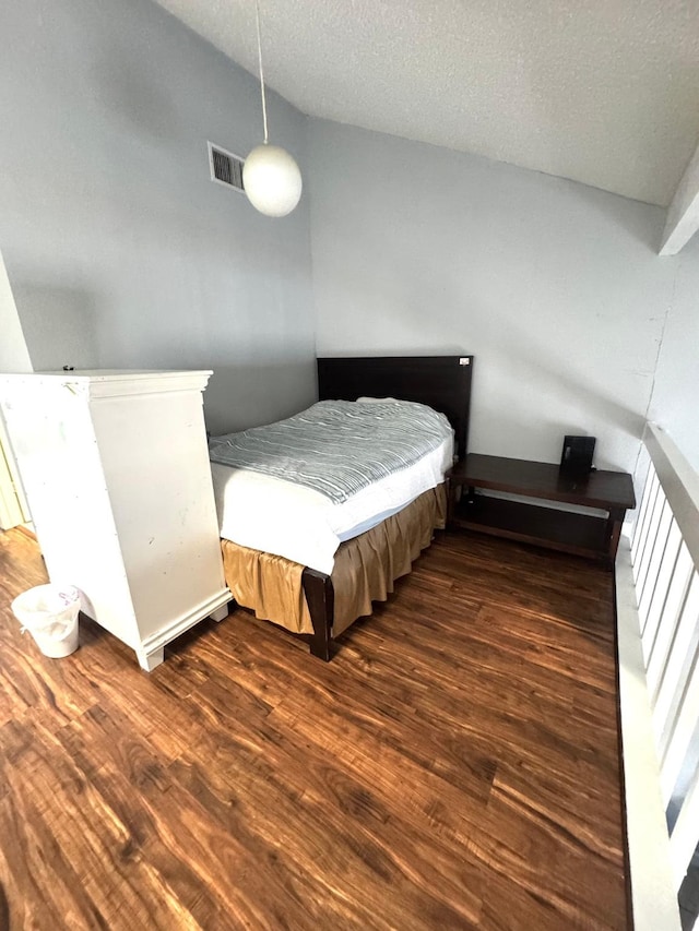 bedroom with a textured ceiling, vaulted ceiling, and dark wood-type flooring