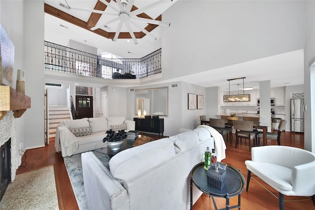 living room with a stone fireplace, ceiling fan, a towering ceiling, and wood-type flooring