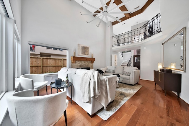 living room featuring a stone fireplace, ceiling fan, wood-type flooring, and a high ceiling