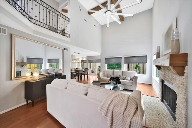 living room featuring ceiling fan, a stone fireplace, beamed ceiling, high vaulted ceiling, and wood-type flooring