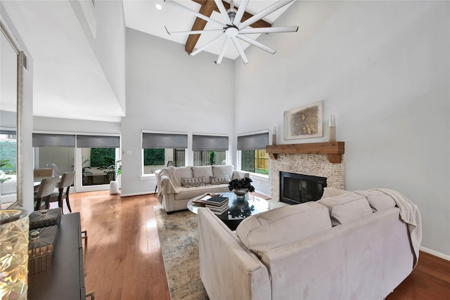 living room with ceiling fan, beamed ceiling, high vaulted ceiling, a fireplace, and hardwood / wood-style flooring