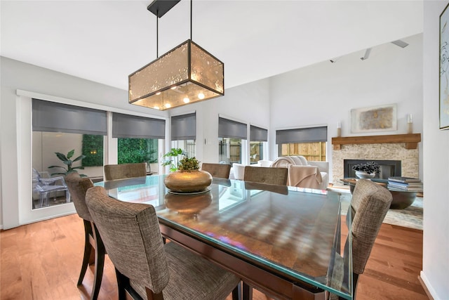 dining room featuring light wood-type flooring, a stone fireplace, and a wealth of natural light