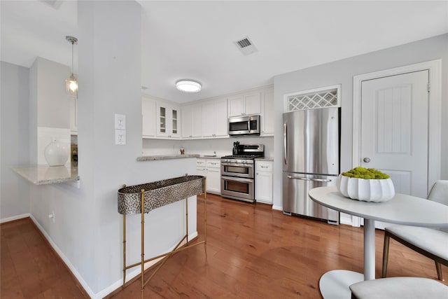 kitchen featuring pendant lighting, dark hardwood / wood-style floors, appliances with stainless steel finishes, light stone counters, and white cabinetry