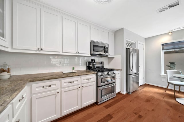 kitchen with hardwood / wood-style floors, dark stone counters, decorative backsplash, white cabinets, and appliances with stainless steel finishes