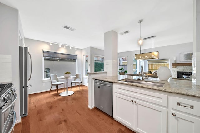 kitchen with light stone countertops, white cabinetry, sink, stainless steel appliances, and light wood-type flooring