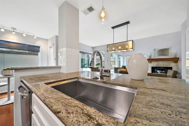 kitchen with sink, light stone counters, wood-type flooring, decorative light fixtures, and a fireplace