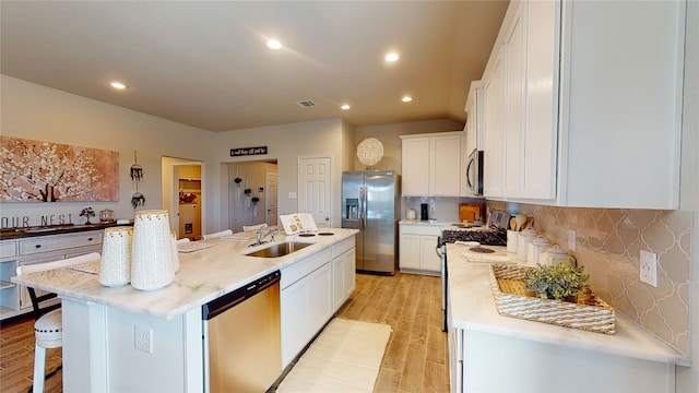 kitchen with white cabinetry, sink, stainless steel appliances, a center island with sink, and light wood-type flooring