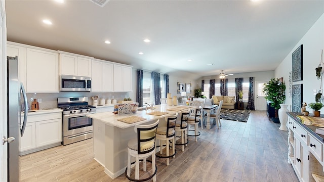 kitchen with a kitchen bar, stainless steel appliances, a center island with sink, white cabinets, and light hardwood / wood-style floors