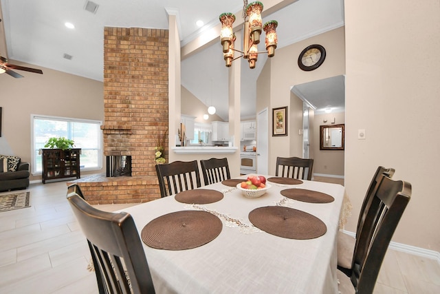 dining room with a brick fireplace, high vaulted ceiling, ornamental molding, and ceiling fan with notable chandelier