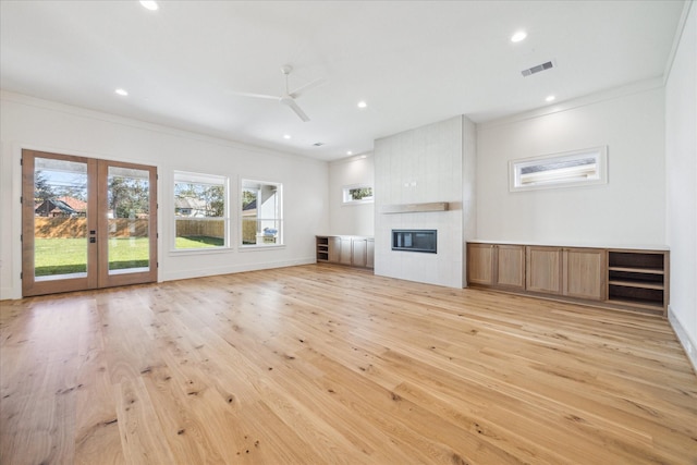 unfurnished living room featuring light hardwood / wood-style flooring, ceiling fan, ornamental molding, a tiled fireplace, and french doors