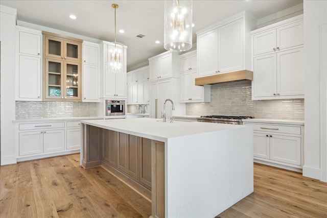 kitchen with a kitchen island with sink, oven, white cabinetry, light countertops, and light wood finished floors