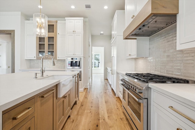 kitchen with light wood-style floors, high quality appliances, light countertops, wall chimney range hood, and a sink