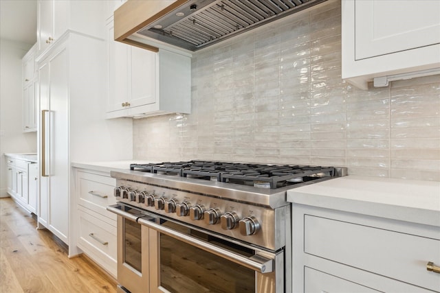 kitchen featuring white cabinetry, tasteful backsplash, light wood-type flooring, double oven range, and custom range hood