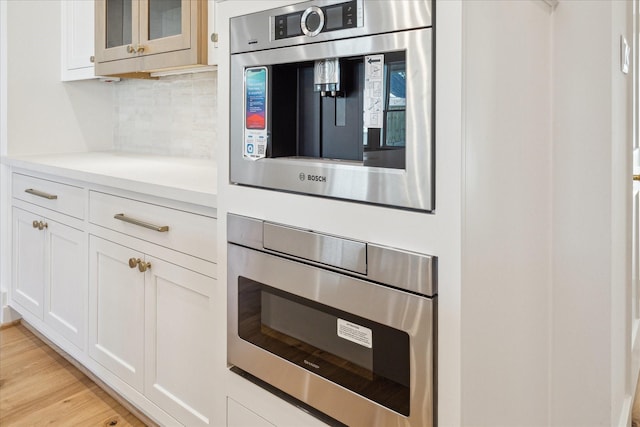 kitchen featuring oven, light countertops, decorative backsplash, light wood finished floors, and glass insert cabinets