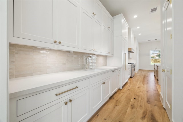 bar featuring visible vents, decorative backsplash, high end range, light wood-style floors, and a sink