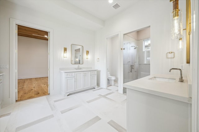 bathroom featuring toilet, a stall shower, two vanities, and a sink