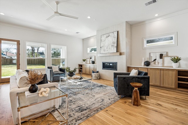 living room featuring light wood-type flooring, visible vents, a tiled fireplace, and recessed lighting