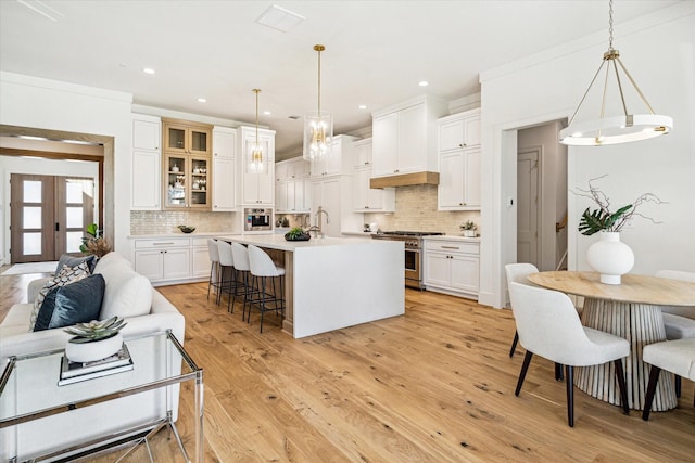 kitchen with light wood-style floors, white cabinetry, a center island with sink, and high end stainless steel range