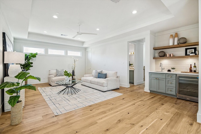 living area featuring light wood finished floors, wine cooler, a raised ceiling, and wet bar