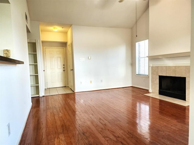 unfurnished living room featuring a tile fireplace, light wood-type flooring, and lofted ceiling