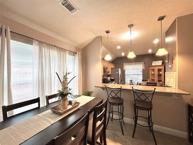 kitchen featuring hanging light fixtures, kitchen peninsula, stainless steel fridge, lofted ceiling, and a breakfast bar