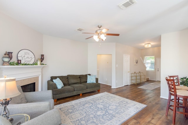 living room featuring a fireplace, ceiling fan, and dark wood-type flooring