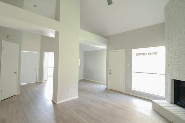 unfurnished living room with light hardwood / wood-style floors, a towering ceiling, and a brick fireplace