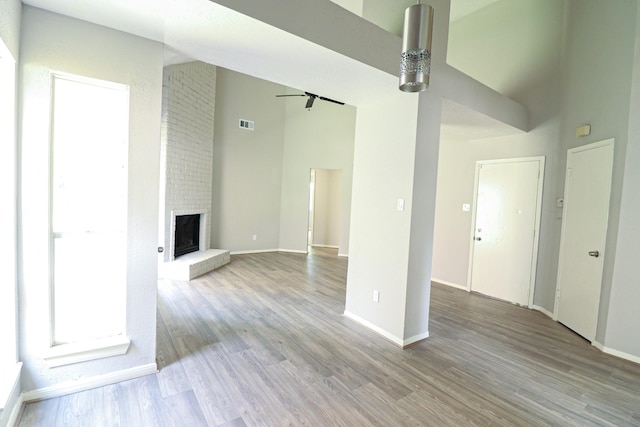 unfurnished living room with ceiling fan, light hardwood / wood-style flooring, a high ceiling, and a brick fireplace