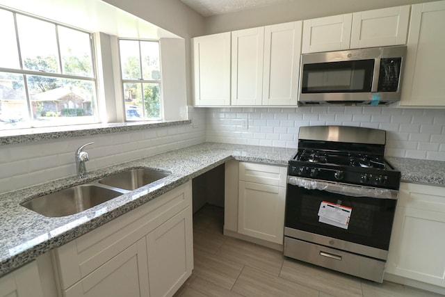 kitchen with decorative backsplash, light stone countertops, sink, and appliances with stainless steel finishes