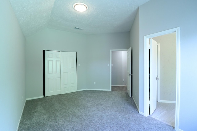 unfurnished bedroom with carpet, a closet, a textured ceiling, and vaulted ceiling