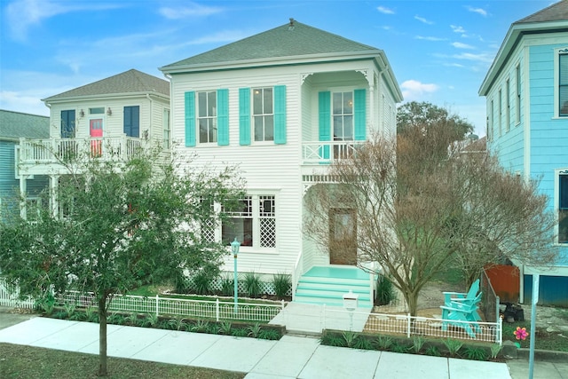 view of front of home with a fenced front yard, roof with shingles, and a balcony