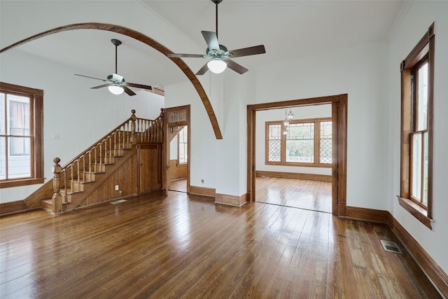 unfurnished living room with arched walkways, hardwood / wood-style flooring, visible vents, baseboards, and stairway